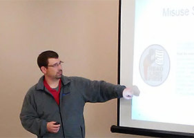 Man in a grey jacket pointing to a presentation screen.